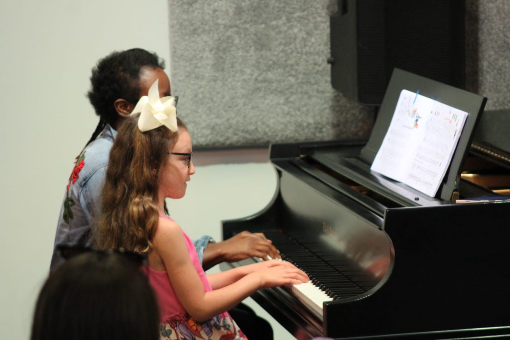 A piano teacher and piano student playing a piano duet at a music recital learning valuable life long skills through music.