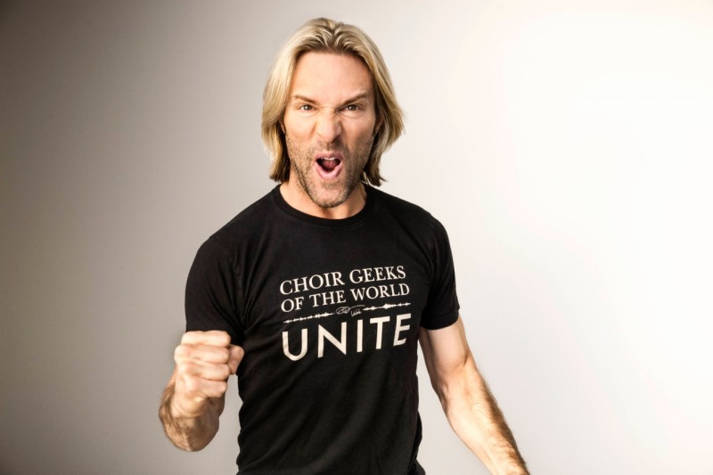 Composer Eric Whitacre smiling alongside a group of choral singers and music students.