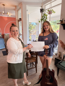 Music instructor and student smiling together inside Chambers Music Studio while holding a certificate of achievement next to an acoustic guitar.